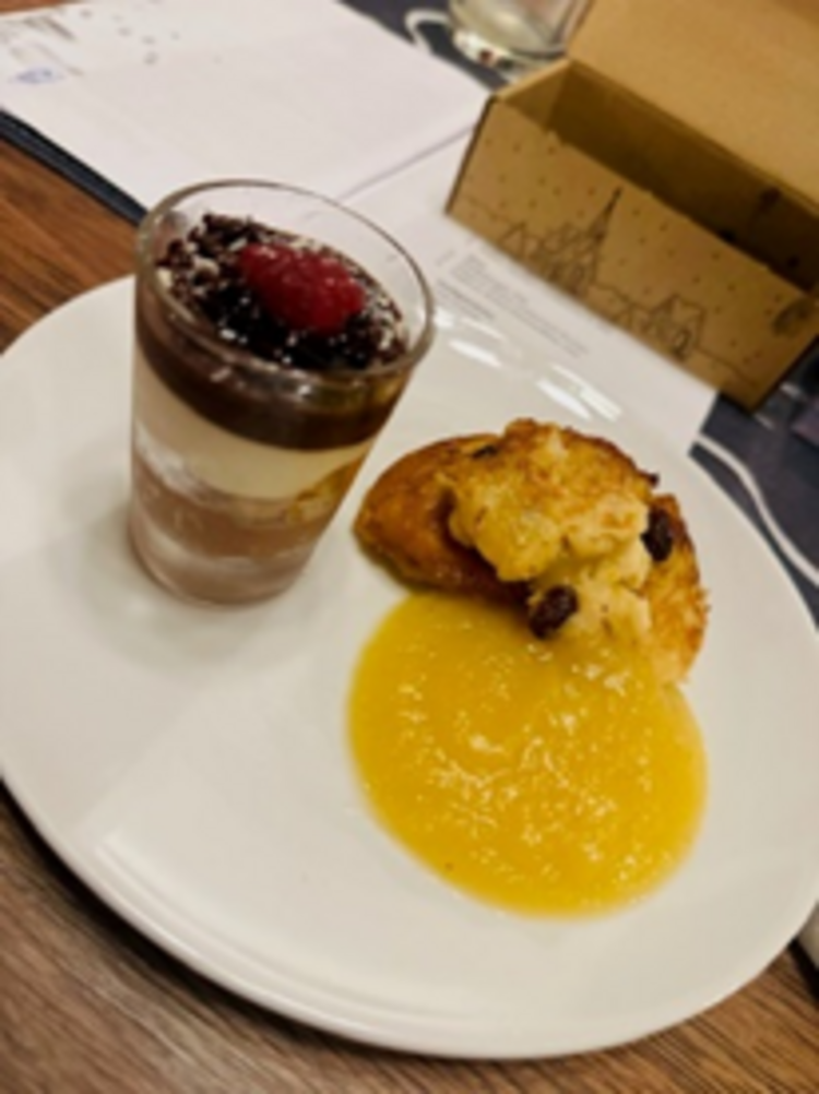Räucherkerzen und ein Hauch von Weihnacht Weißer Dessertteller mit einem geschichteten Schokoladencreme-Glas mit Himbeere und einem Stück süßem Auflauf oder Hefezopf, serviert mit gelber Fruchtsauce.