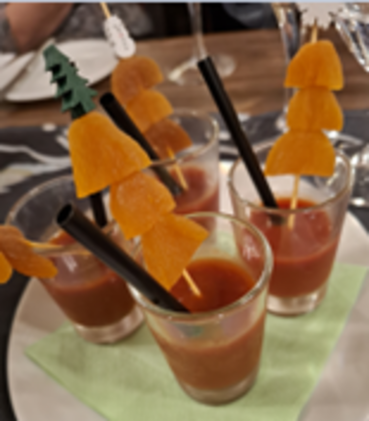 Räucherkerzen und ein Hauch von Weihnacht Kleine Gläser mit roter Suppe oder Drink, in denen schwarze Trinkhalme und Holzspieße mit in Stücke geschnittenen getrockneten Aprikosen stecken, auf einer grünen Serviette angerichtet.