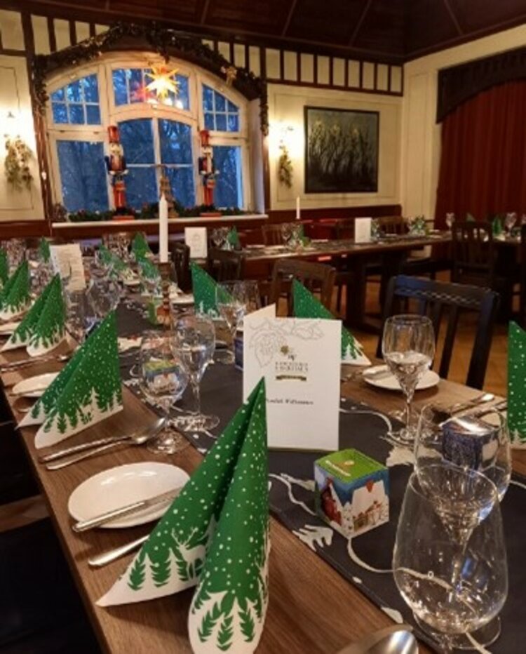 Räucherkerzen und ein Hauch von Weihnacht Lang eingedeckter Festtisch im Jugendstilsaal mit grünen Tannenbaum-Servietten, Menükarten, Gläsern und Kerzen, dekoriert für eine Weihnachtsfeier.