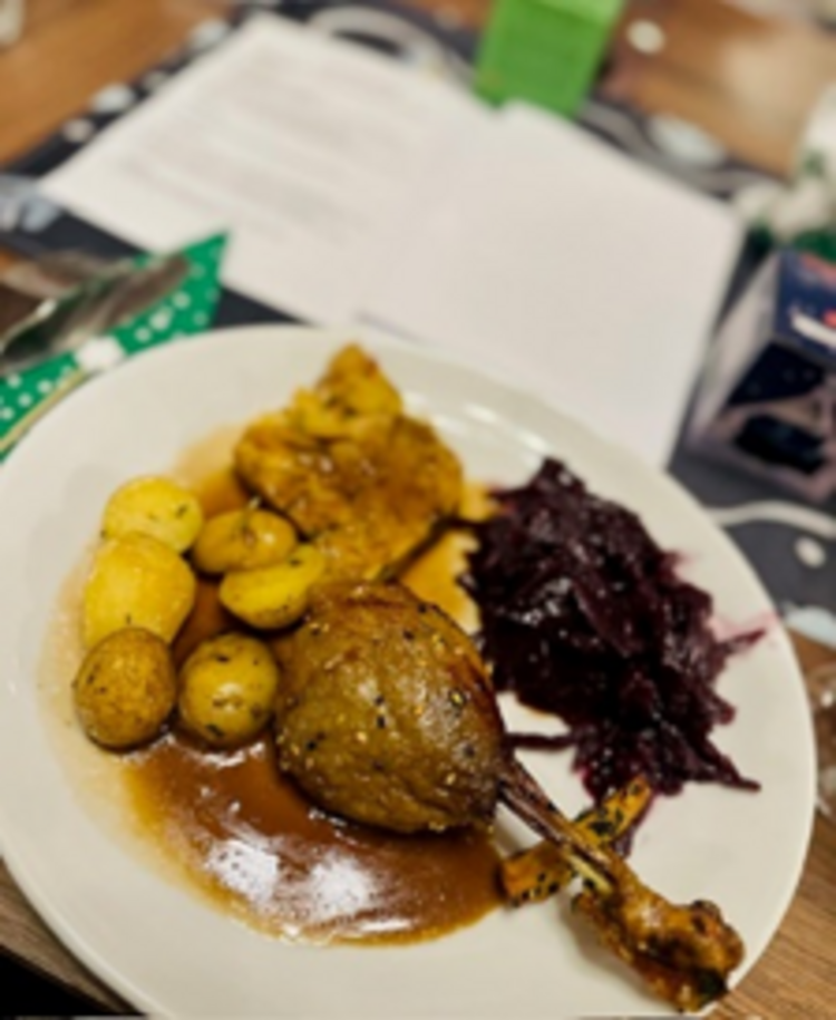Räucherkerzen und ein Hauch von Weihnacht Hauptgericht auf einem weißen Teller mit knuspriger Gänsekeule, Bratkartoffeln, Rotkohl und brauner Soße, auf einem festlich gedeckten Tisch.